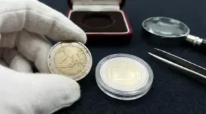 Monete rare maneggiate con guanti bianchi accanto a lente d'ingrandimento e pinzette