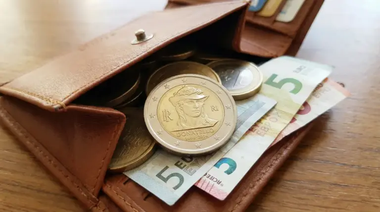 Portafoglio aperto con monete da due euro, tra cui una dedicata a Donatello, e banconote da cinque euro