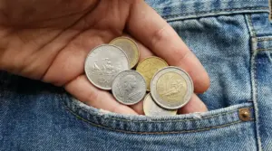 Mano che tiene diverse monete, inclusi pezzi in euro e lire italiane, sopra una tasca di jeans