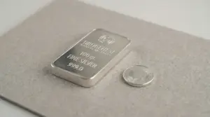 Lingotto d'argento da 100 grammi accanto a una moneta su una superficie chiara