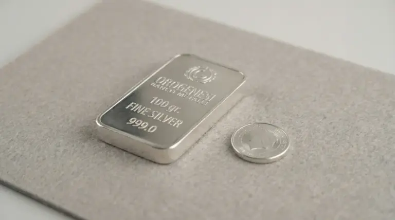 Lingotto d'argento da 100 grammi accanto a una moneta su una superficie chiara