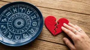 Mano accanto a un cuore spezzato e un piatto con simboli dello zodiaco su tavolo in legno